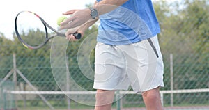 Midsection of caucasian male tennis player hitting ball with racket at outdoor court in slow motion