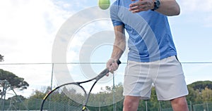 Midsection of caucasian male tennis player hitting ball with racket at outdoor court in slow motion