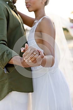 Midsection of caucasian newlywed couple holding hands and dancing at wedding ceremony at beach