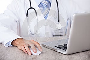 Midsection of doctor using laptop and mouse at desk