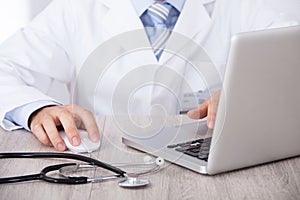 Midsection of doctor using laptop and mouse at desk