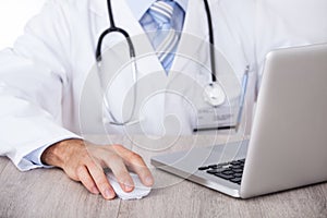 Midsection of doctor using laptop and mouse at desk photo