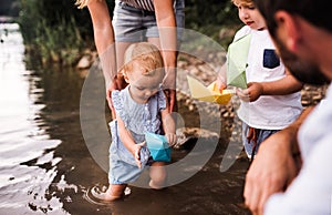 A midsection of family with two toddler children outdoors by the river in summer.
