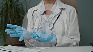 Midsection of female doctor putting medical protective gloves indoors