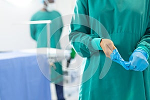 Midsection of female surgeon in surgical gown taking off gloves in operating theatre, copy space