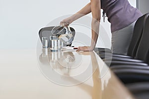 Midsection Of Female Worker Pouring Water Into Glasses On Confer photo