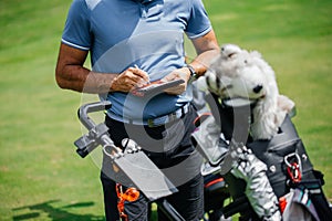 Midsection of golfer writing on score card standing at golf course