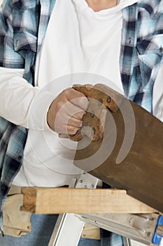 Midsection of male construction worker cutting wood with handsaw