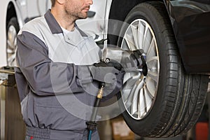 Midsection of male mechanic repairing car's wheel in workshop