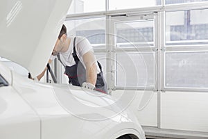 Midsection of male technician repairing car engine in workshop