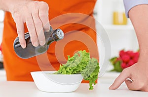 Midsection of a man pouring olive oil over fresh salad in restaurant kitchen. Concept of healthy eating