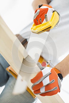 Midsection of man sawing plank