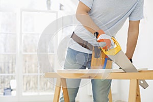 Midsection of man sawing wood in new house