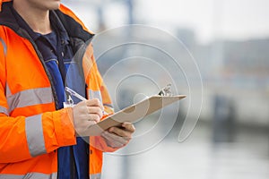 Midsection of mid adult man writing on clipboard in shipping yard