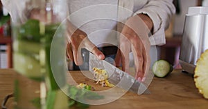 Midsection of mixed race woman preparing health drink chopping pineapple in cottage kitchen