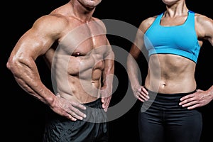 Midsection of muscular man and woman with hands on hip