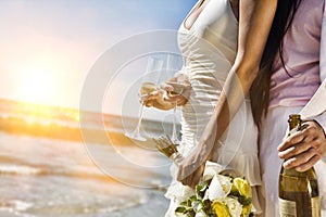 Midsection of newlywed couple with champagne bottle and flutes on beach