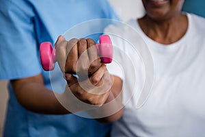 Midsection of nurse guiding senior woman in lifting dumbbell