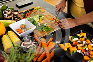 Midsection of plus size african american woman preparing dinner, chopping vegetables in kitchen