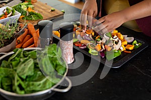 Midsection of plus size african american woman preparing dinner, seasoning vegetables in kitchen