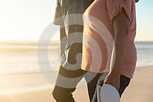 Midsection of retired senior african american couple walking at beach during sunset