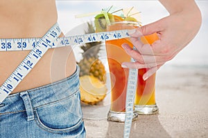 Midsection section of woman measuring waist with juices in background