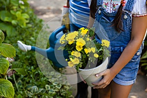 Midsection of senior woman and granddaughter holding watering can and yellow flower pot