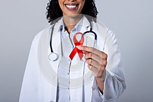 Midsection of smiling african american mid adult female doctor holding red aids awareness ribbon