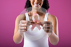 Midsection of smiling african american mid adult woman holding pink breast cancer awareness ribbon