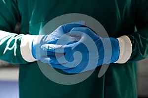 Midsection of surgeon in blue gloves and green gown in operating theatre