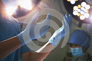 Midsection view of hands in surgical gloves and surgical lights in the operating room