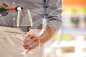 Midsection of waiter pouring red wine in wineglass at restaurant