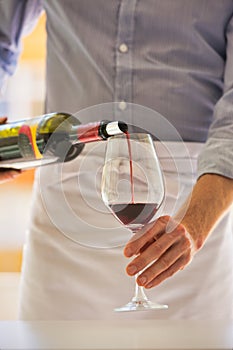 Midsection of waiter pouring red wine in wineglass at restaurant