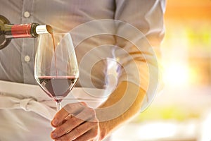 Midsection of waiter pouring red wine in wineglass at restaurant