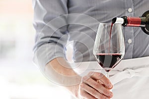 Midsection of waiter pouring red wine in wineglass at restaurant