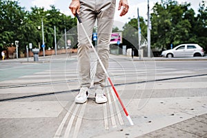 Midsection of young blind man with white cane walking across the street in city.