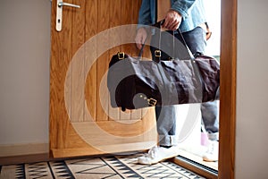 Midsection of young man with bag entering front door when coming back home.