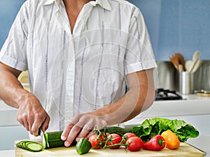 Midsection of young man cutting vegetables on wooden board in domestic kitchen