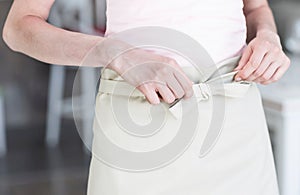 Midsection of young waitress tying apron while standing at restaurant