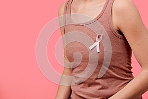 Midsection of a young woman wearing pink breast cancer awareness ribbon isolated over living coral background.
