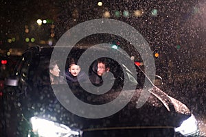 In the midst of a nighttime journey, a happy family enjoys playful moments inside a car as they travel through rainy