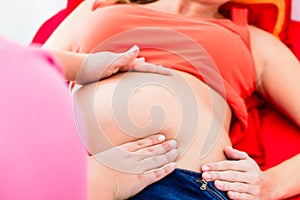 Midwife exanimating belly of pregnant woman manually photo