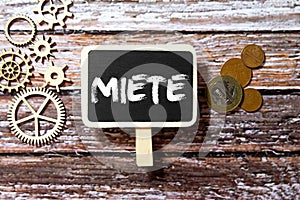 Miete in German language, white chalk type on black board, Euro money coin stacks of growth on wood table