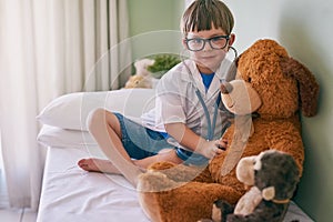 This might lead to a career in medicine. a little boy pretending to be a doctor while examining his teddybear.