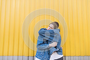 Mighty hugs on the background of a yellow wall.Stylish young couple hugging on a lively background