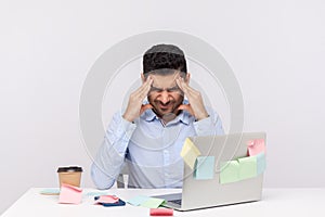 Migraine of stressful job. Depressed man employee sitting in office, clasping head temples, suffering headache