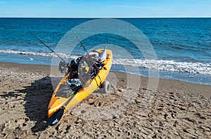 Orange sea kayak with fishing equipment and a caught fish on Cala de Mijas beach.