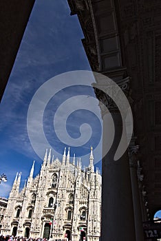 Milan Cathedral facade with  blue sky.  In the foreground the arches of the portico