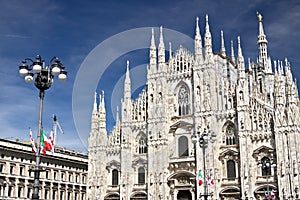 Milan Cathedral facade with flags on blue sky. Flags waving on the blue sky