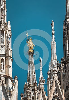 Milan Cathedral spires, Italy. Golden statue of Madonna on blue sky background. Famous Milan Cathedral or Duomo di Milano is top